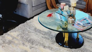 Ein modernes Wohnzimmer mit einem grauen Ecksofa, einem Glastisch und einem großen abstrakten Gemälde an der Wand.