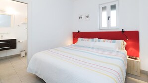 A bedroom with a bed, a red headboard, a window, and a bathroom with a mirror and sink. - Alhambra View Suite Apartamentos Bravo (Granada)