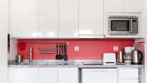 A modern kitchen with white cabinets, a red backsplash, and stainless steel appliances including a microwave and coffee maker. - Alhambra View Suite Apartamentos Bravo (Granada)