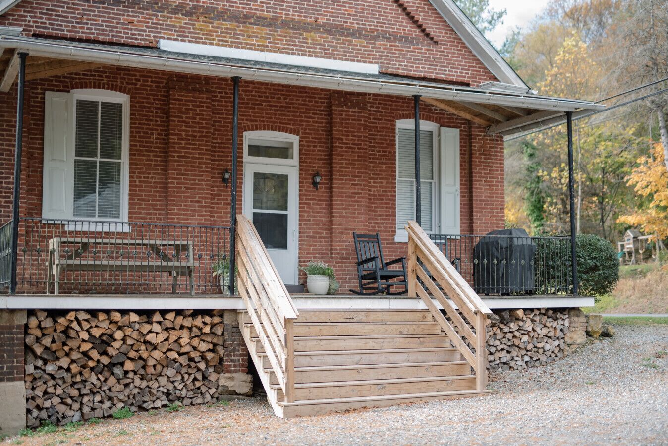 A brick house with a porch, a wooden staircase, and a bench.