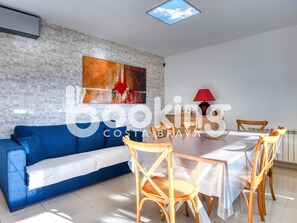 Una sala de estar moderna con un sofá azul, una mesa de comedor con cuatro sillas y una lámpara roja.