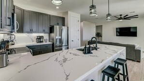 Een moderne keuken met een marmeren eiland, roestvrijstalen apparatuur en hangende lampen.