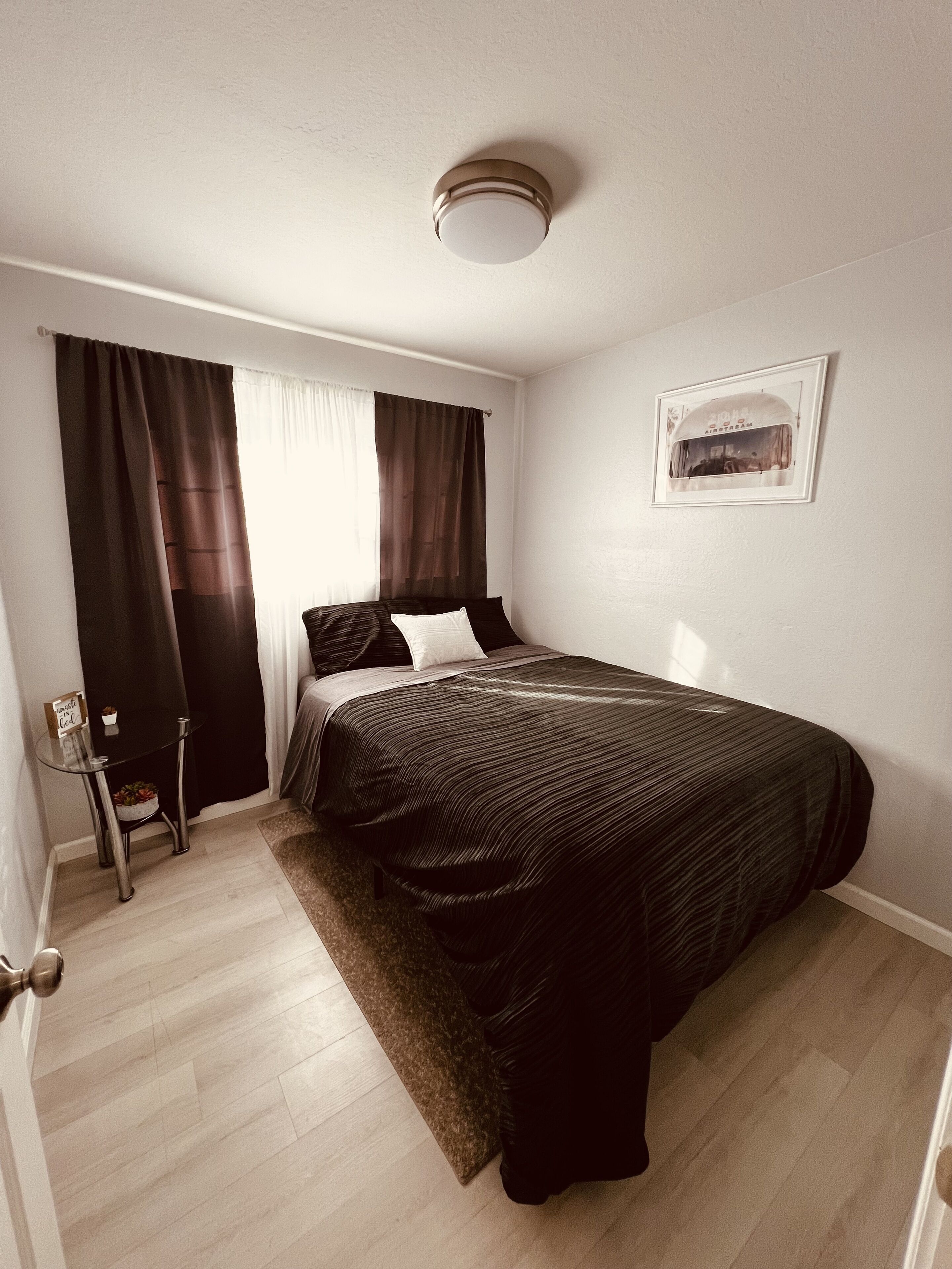 A bedroom with a bed, curtains, a round table, and a picture on the wall.