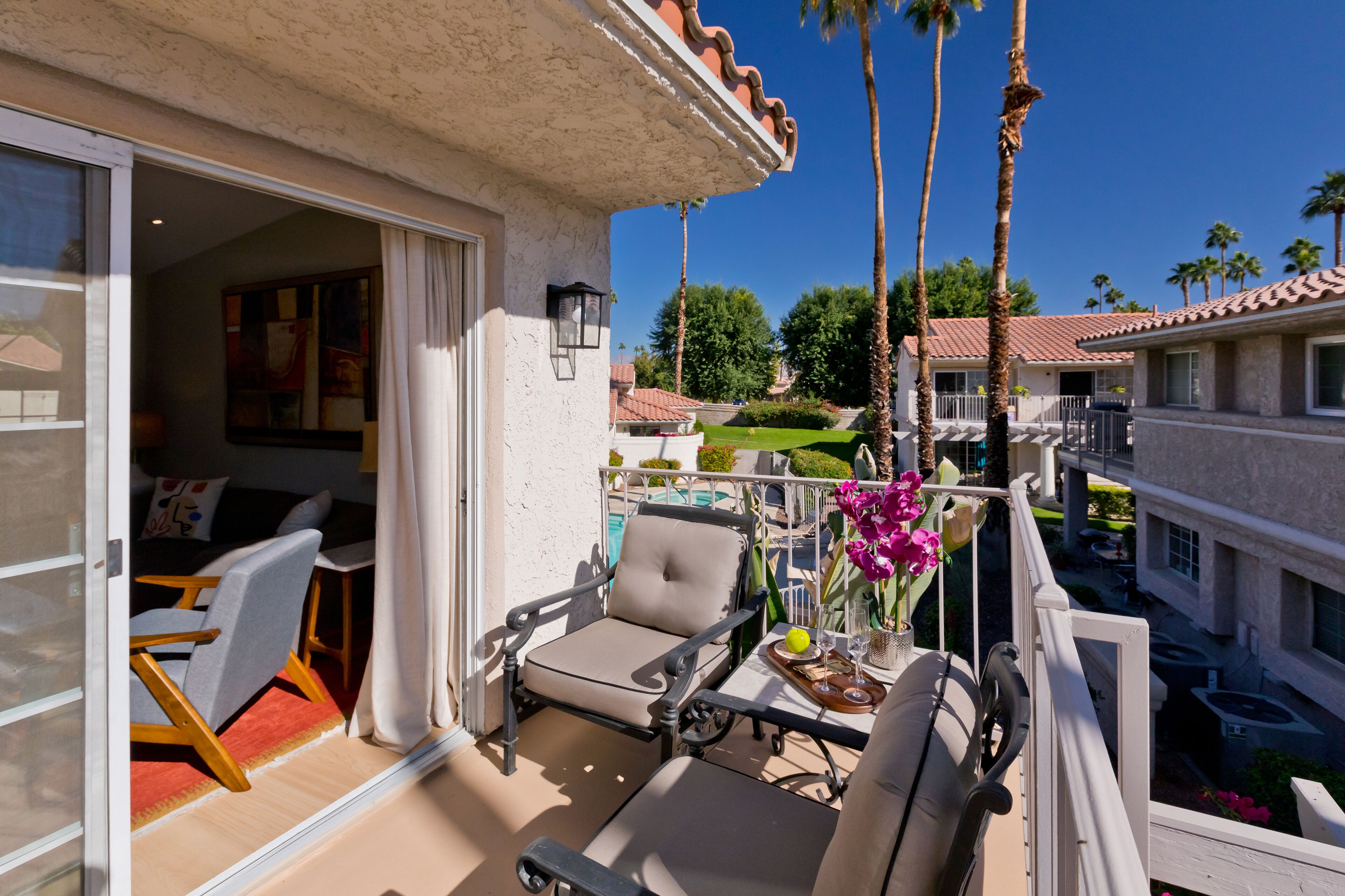 Un balcon aménagé avec du mobilier d’extérieur, une piscine et des palmiers.