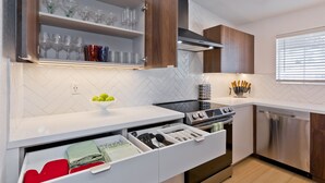 A modern kitchen with white cabinetry, a built-in oven, a dishwasher, and a herringbone-patterned backsplash. - Los Balcones de Palm Springs Mid-Century Modern Designer Condo, City ID #068484 (Palm Springs)