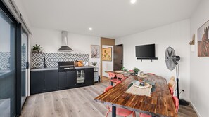 A modern kitchen with a built-in oven, a dining area with a wooden table and red chairs, and a flat-screen TV mounted on the wall. - Number Thirty One Smiths Beach Phillip Island (Smiths Beach)
