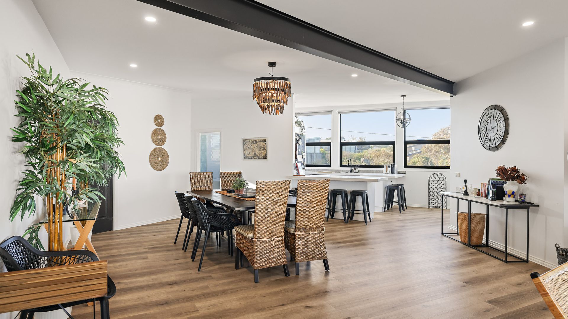 A modern kitchen with a dining area, featuring a large window, a hanging light fixture, and a bamboo plant.