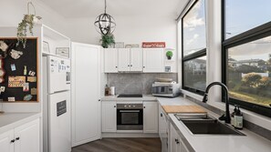 A modern kitchen with white cabinets, a black countertop, a built-in oven, a microwave, and a window with a view of the neighborhood. - Number Thirty One Smiths Beach Phillip Island (Smiths Beach)