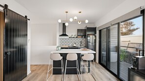 A modern kitchen with a central island, bar stools, and a large window.