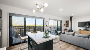A modern kitchen with a central island, a dining area with chairs, a sofa, and a fireplace.