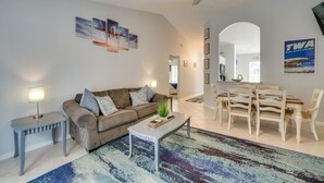 Ein Wohnzimmer mit einer Couch, Couchtisch und Esstisch. Es gibt einen Deckenventilator, einen Teppich und gerahmte Bilder an der Wand.