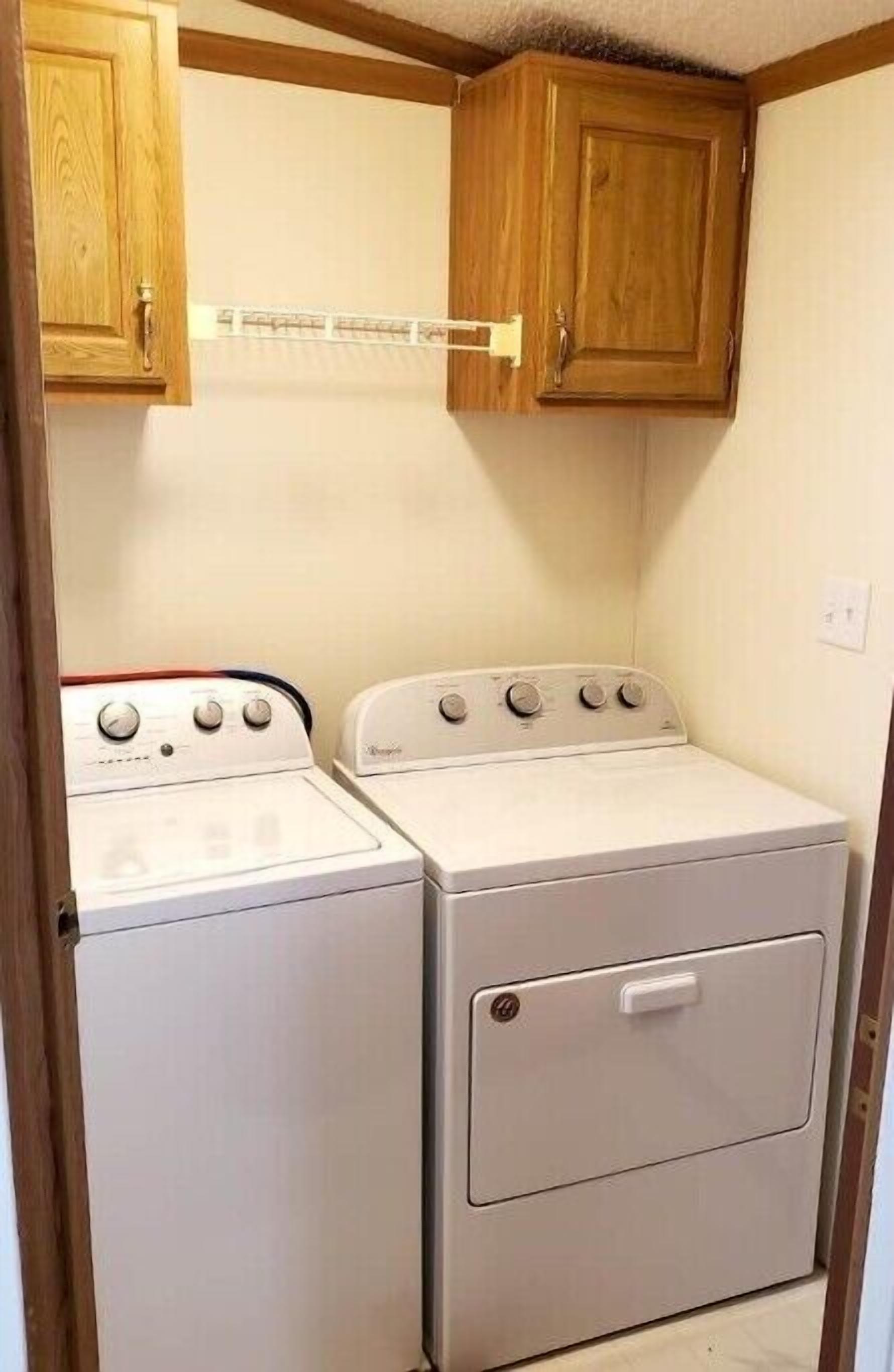 A laundry room with two washing machines and wooden cabinets above.