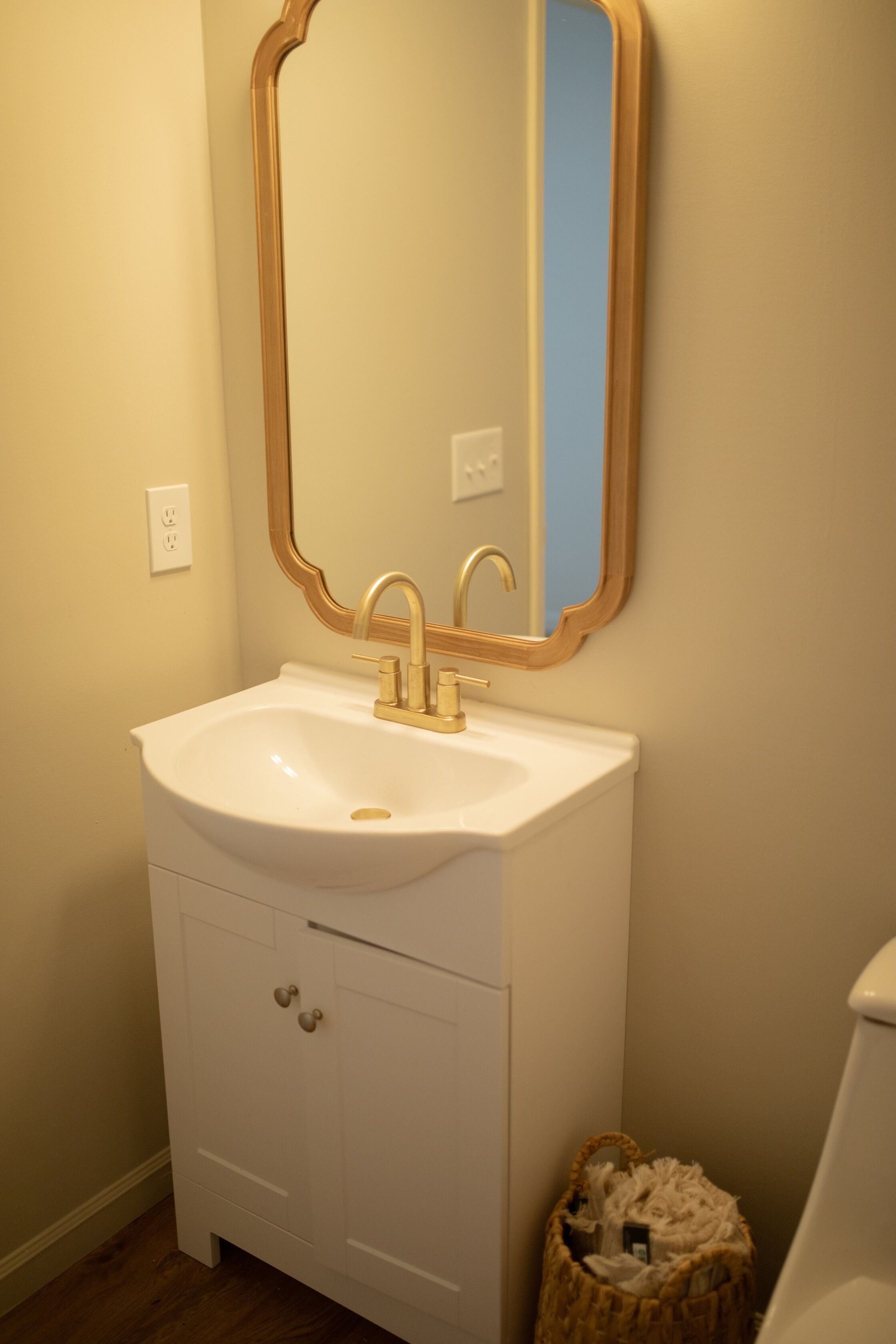 A bathroom with a white sink, gold faucets, and a mirror with a gold frame.