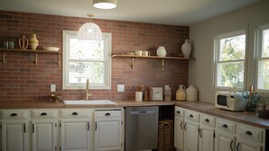Una cocina con armarios blancos, pared de ladrillo, ventana y microondas.