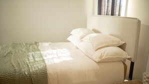 Una cama bien hecha con una manta verde, un cabecero blanco y una taza a cuadros sobre una mesita de noche.