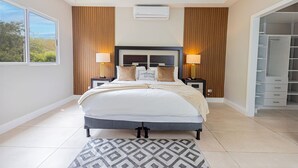 Een moderne slaapkamer met een groot bed, nachtlampjes, een inbouwkast en uitzicht op groen.