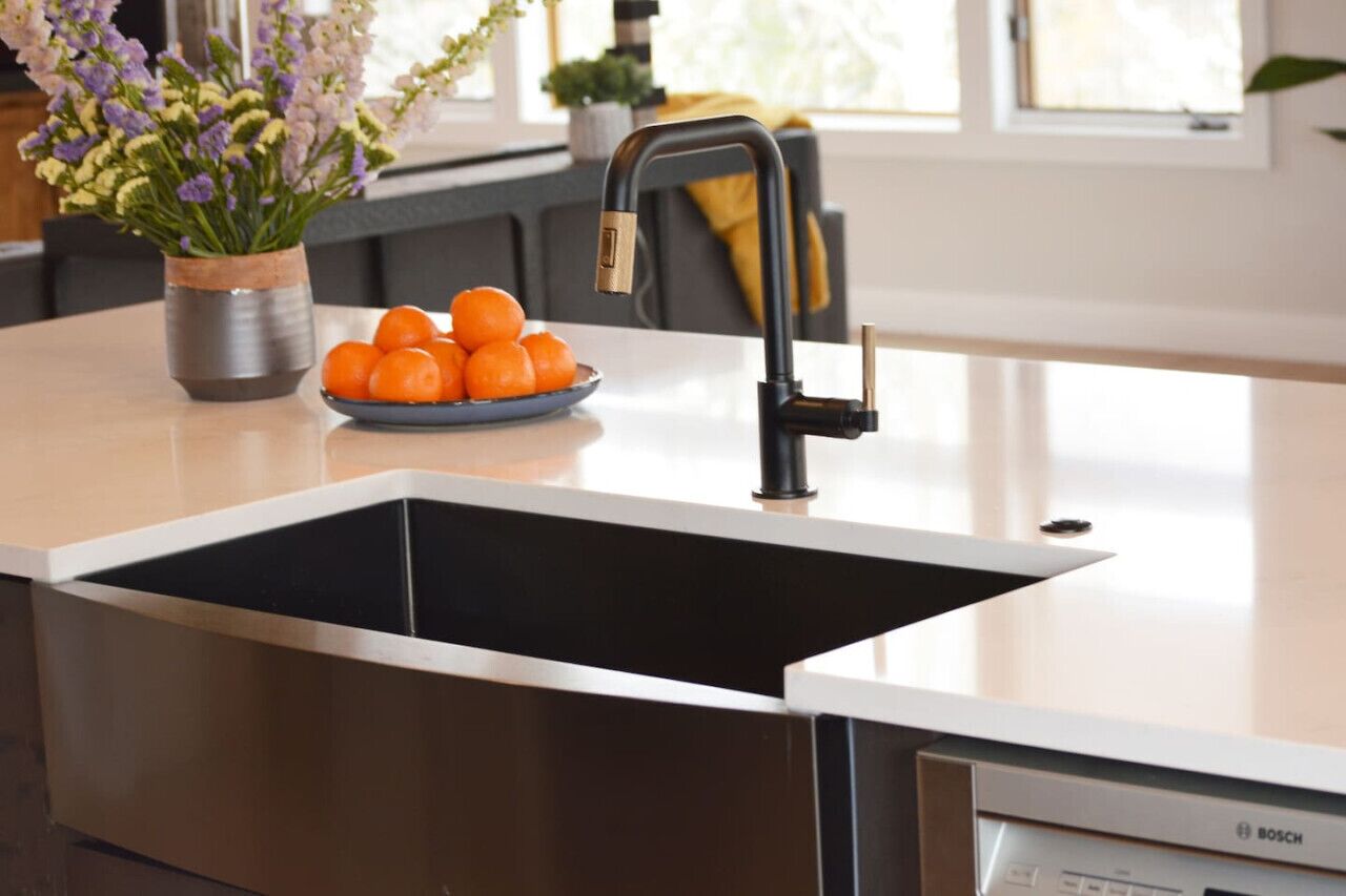 Une cuisine équipée d’un lave-vaisselle Bosch, d’un robinet noir et d’un saladier rempli d’oranges posé sur le plan de travail.