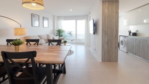 Une cuisine moderne équipée d’un lave-linge intégré, un coin repas avec une table et des chaises en bois, et une grande fenêtre qui laisse entrer la lumière naturelle.