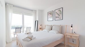 Une chambre à coucher au style minimaliste, avec un grand lit, deux tables de chevet, une fenêtre avec des rideaux et deux tableaux encadrés accrochés au mur.