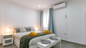 A modern bedroom with a bed, bedside tables, a bench, and an air conditioning unit. - Cozy apartment in Sanlúcar de Barrameda (Sanlúcar de Barrameda)