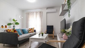 A modern living room with a grey sofa, a black armchair, a white coffee table, and a TV. There is a potted plant on the sofa and another on the coffee table. - Cozy apartment in Sanlúcar de Barrameda (Sanlúcar de Barrameda)