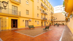 A courtyard with yellow buildings, benches, and a tiled floor. - Cozy apartment in Sanlúcar de Barrameda (Sanlúcar de Barrameda)