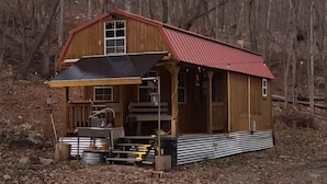 A wooden cabin with a red roof, a porch, and a chimney.