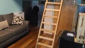 A room with a wooden floor, a sofa, a ladder, and a black cabinet.