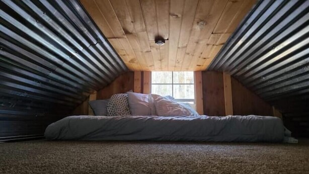 A small attic bedroom with a sloped ceiling, a single bed, and a window.