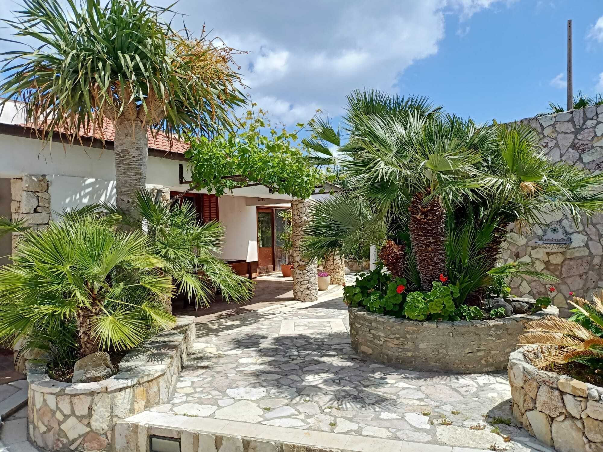 Un patio con suelo de piedra, palmeras y un muro de piedra con un detalle decorativo.