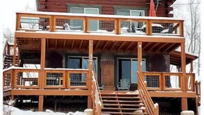 A multi-story wooden cabin with a balcony on the second floor, a chimney, and a staircase leading to the entrance. - Cozy Cabin with Private Hot Tub and Stunning Views (Silverthorne)