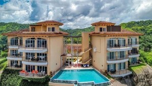 Un edificio a due piani con piscina, balconi e vista sul verde circostante.