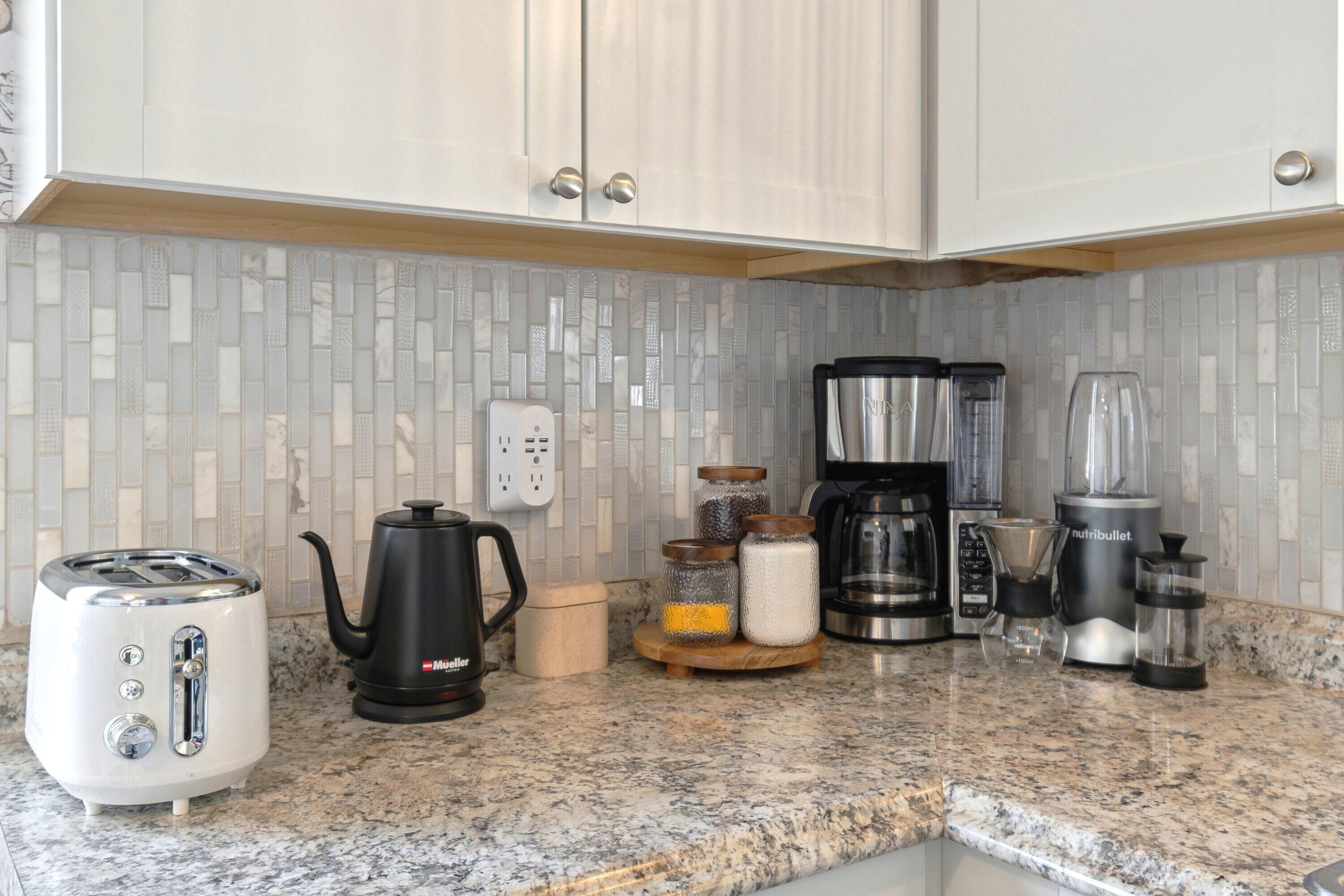 A kitchen with a toaster, a coffee maker, a blender, and a kettle on a granite countertop.