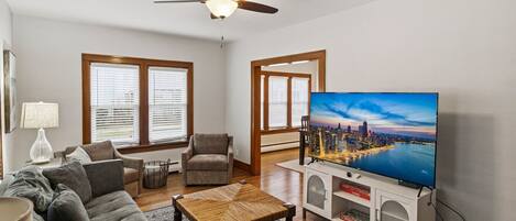 A living room with a sofa, chairs, a coffee table, a TV, and a ceiling fan.