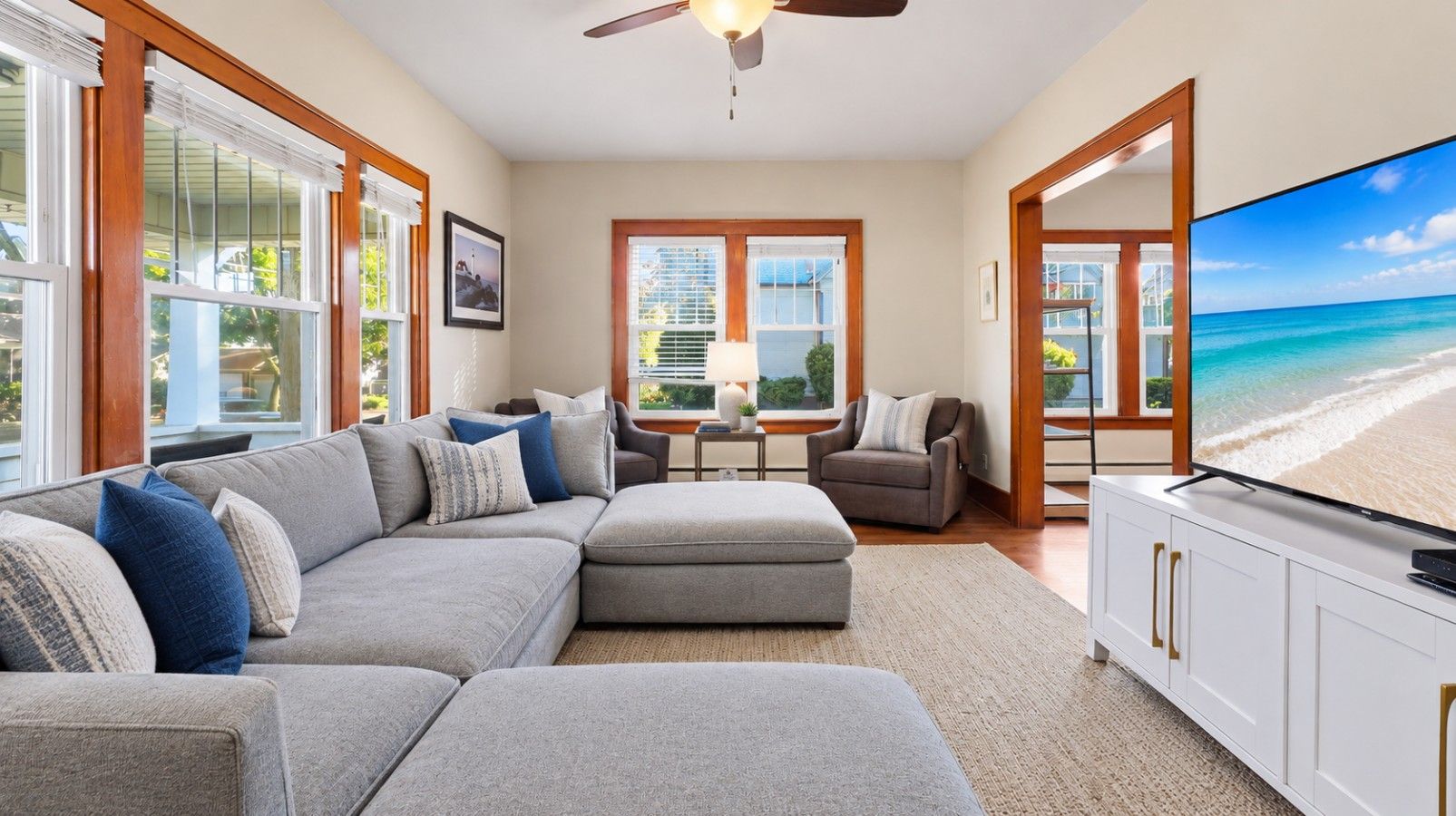 A living room with a sectional sofa, a television, and a view of the beach.