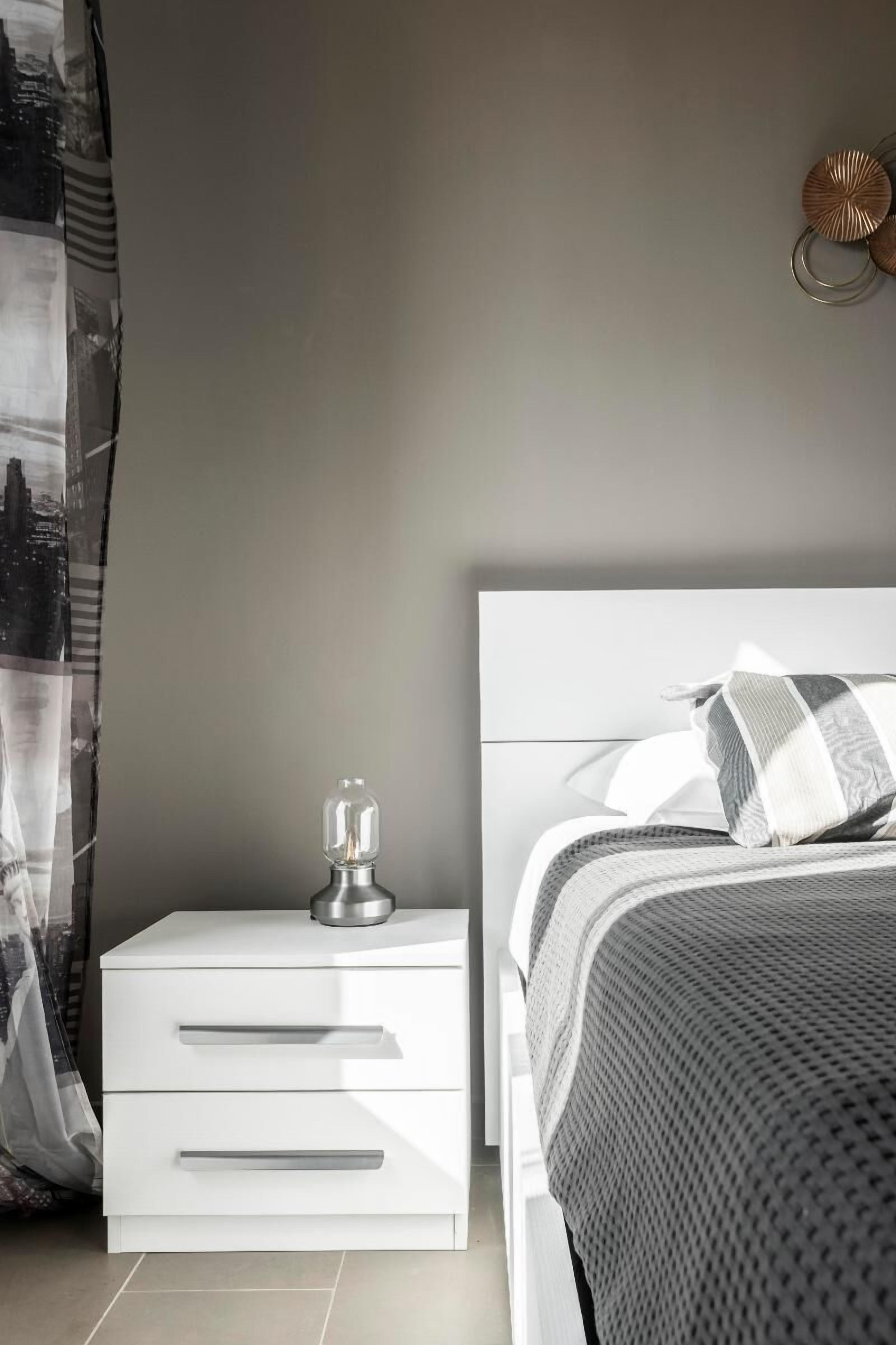Un dormitorio moderno con una mesita de noche blanca, una cama con colcha estampada y una lámpara de pared.