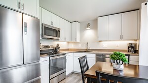Une cuisine moderne dotée d’appareils électroménagers en acier inoxydable, de meubles blancs et d’une table à manger en bois agrémentée d’une plante en pot.