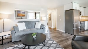 Un salon moderne avec un canapé gris, une table basse noire et un téléviseur fixé au mur au-dessus.