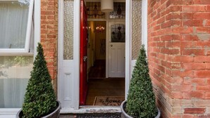 A brick building entrance with a red door, a white door, and a small porch area with two potted plants. - Rustic Revived Victorian Seaside Retreat (Bournemouth)