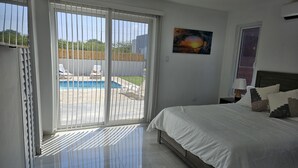 A bedroom with a bed, a ceiling fan, a painting, and a view of a backyard with a pool and chairs. - Aruba Personal Paradise-2BR Home w/ private pool, convenient location (Noord)