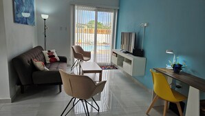 A modern living room with a sofa, chairs, a small table, a TV, and a balcony with a pool view. - Aruba Personal Paradise-2BR Home w/ private pool, convenient location (Noord)