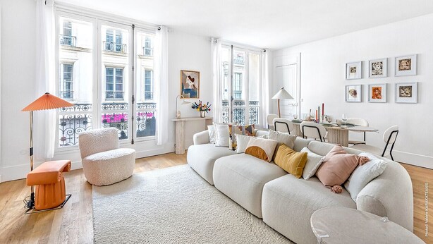 Een moderne woonkamer met een witte bank, een salontafel en een eethoek met een tafel en stoelen.