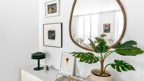 Een minimalistisch ingerichte kamer met een grote ronde spiegel, een lijst met kunstwerk, een potplant en een klein bureau met een lamp.