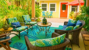 An outdoor patio with wicker furniture, a round table, and a tropical garden setting. - Historical botanical beach house (Lake Worth Beach)