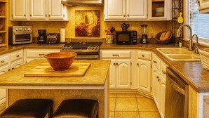 A kitchen with white cabinets, a central island with stools, a stove, microwave, and a sink. - Historical botanical beach house (Lake Worth Beach)