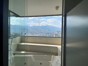 Un balcon avec une porte-fenêtre, une baignoire et une vue sur la ville et les montagnes.