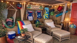 Wicker meubels, een hangmat en een bord met de tekst 'Welcome to Paradise' in een knusse kamer.