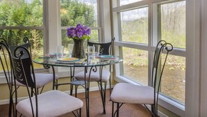 Un coin repas avec une table en verre, quatre chaises et un vase rempli de fleurs violettes.