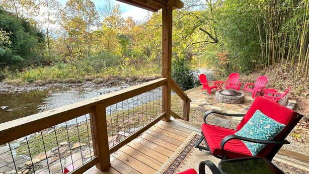 Une terrasse en bois dotée d’une balustrade, qui offre une vue sur une rivière et est entourée d’un feuillage automnal.