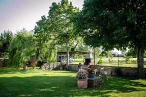 Een tuin met een stenen muur, een houten pergola en een barbecueplaats.
